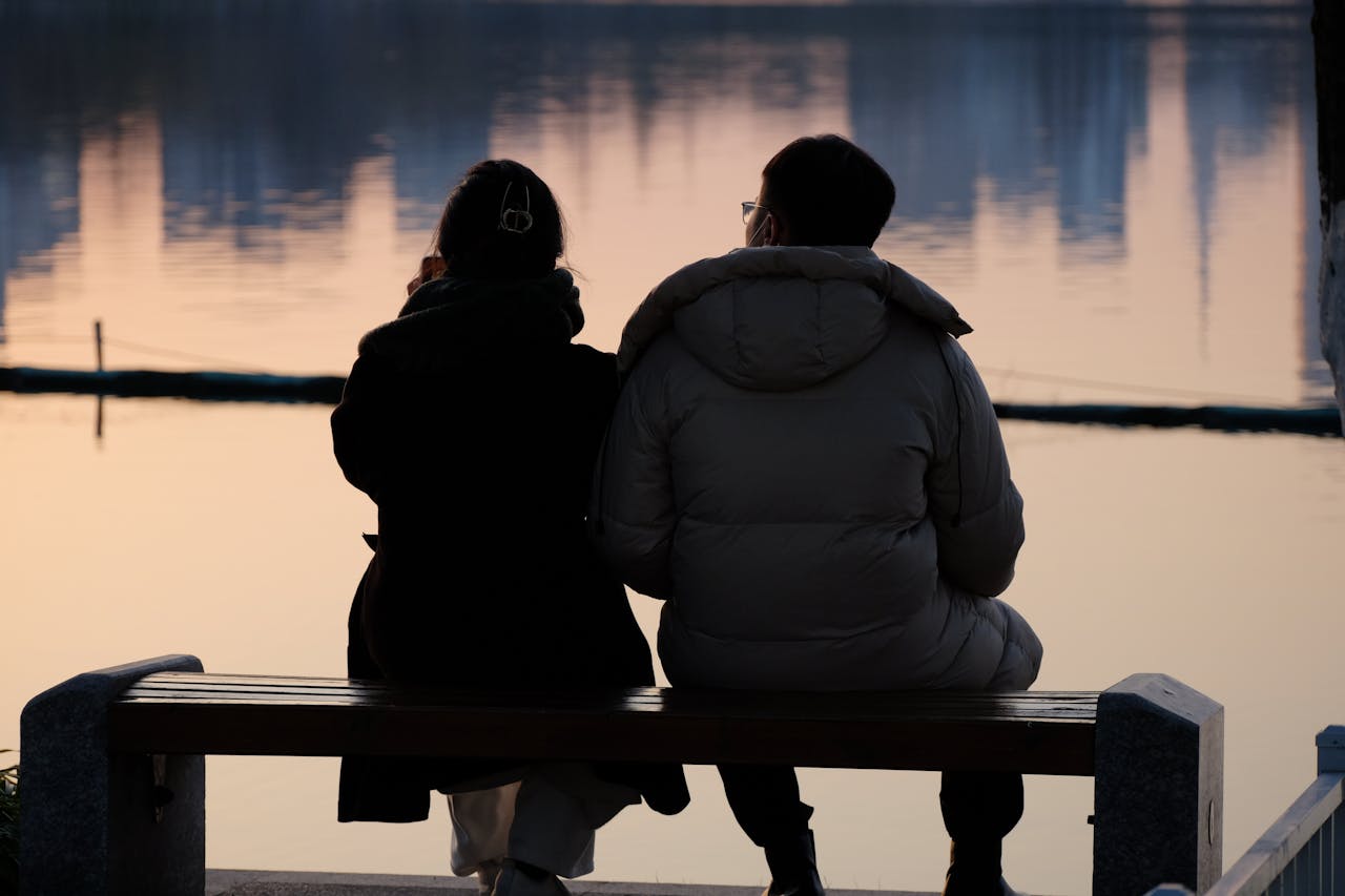 About Serene moment of a couple sitting by the lake, captured at sunset.