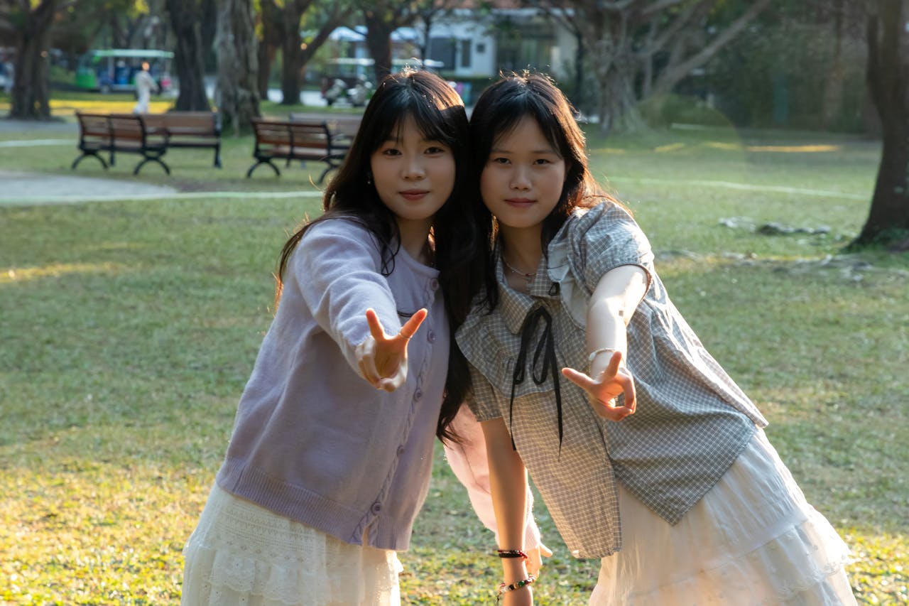 Home Two young women posing with peace signs in a sunny park setting.